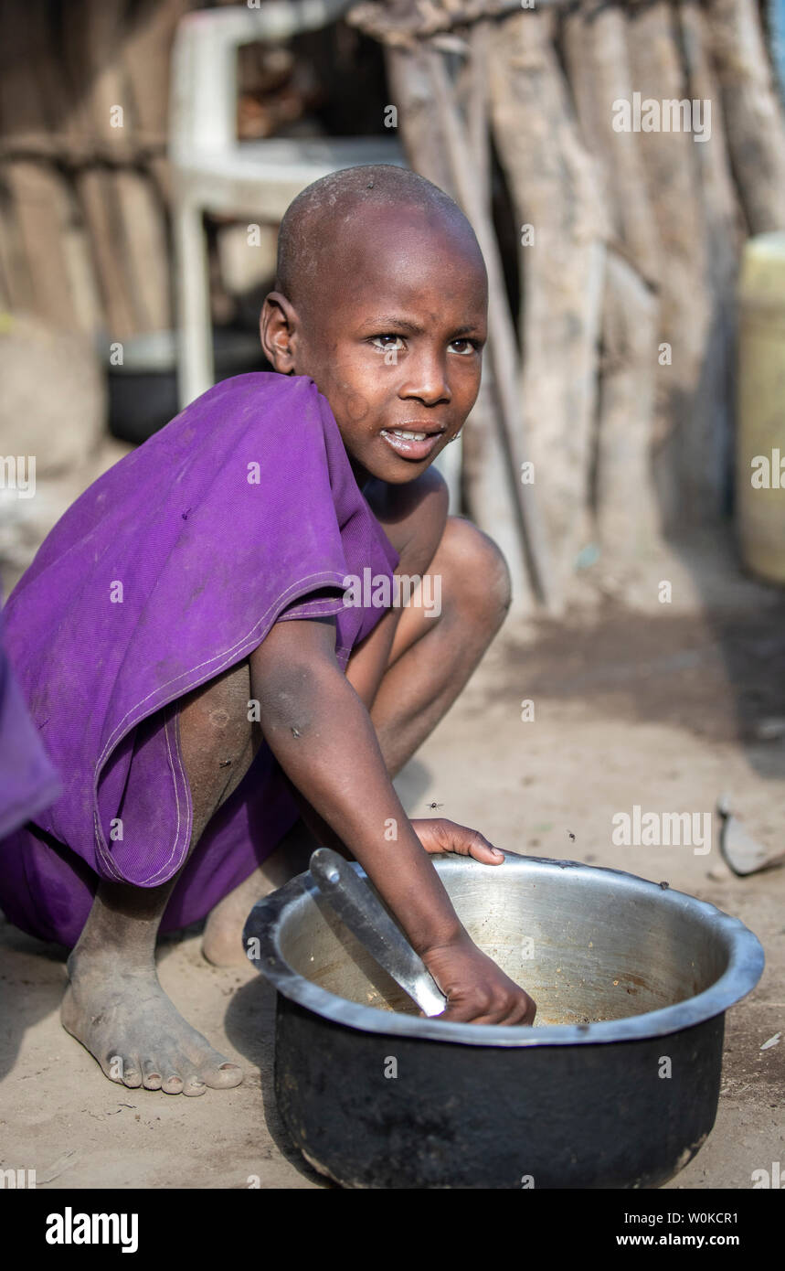 Même, en Tanzanie, 4 juin 2019 : jeune fille Maasai Racler les restes de nourriture sur un pot pour qu'elle puisse manger plus Banque D'Images