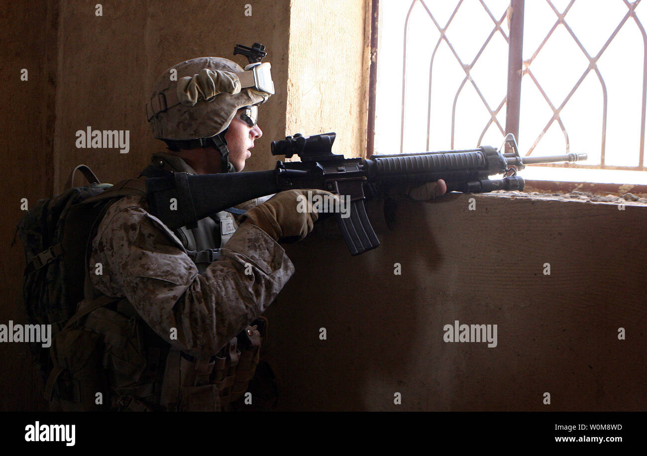 Une des montres marines par une fenêtre tandis que d'autres marines de l'Hawaii, Lima Company, 3e Bataillon, 3e Régiment de Marines, recherchez une maison à Barwana, l'Iraq, de caches d'armes et d'explosifs au cours d'une patrouille dans la ville le 16 juin 2006. Malgré la superbe coup à l'insurrection il y a deux semaines avec la mort d'al-Qaïda en Irak chef Abu Musab al Zarqawi, marines et soldats irakiens dans ce Al Anbar Province ville continuent la lutte contre le terrorisme par la lutte contre les activités des insurgés près de tous les jours. Mais tandis que les Marines et les soldats irakiens patrouillent les rues usées bordée de dépressions Banque D'Images