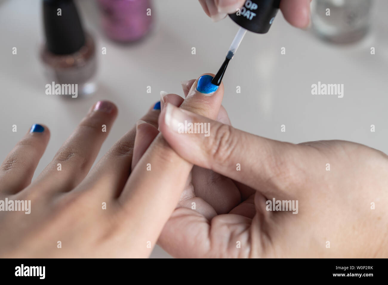 Une mère peint ses mains de jeune fille en bleu et rose nailpolish, considéré dans un cas isolé sur fond blanc Banque D'Images