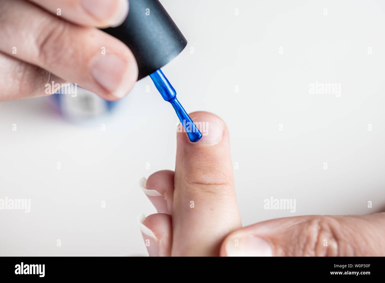 Une mère peint ses mains de jeune fille en bleu et rose nailpolish, considéré dans un cas isolé sur fond blanc Banque D'Images