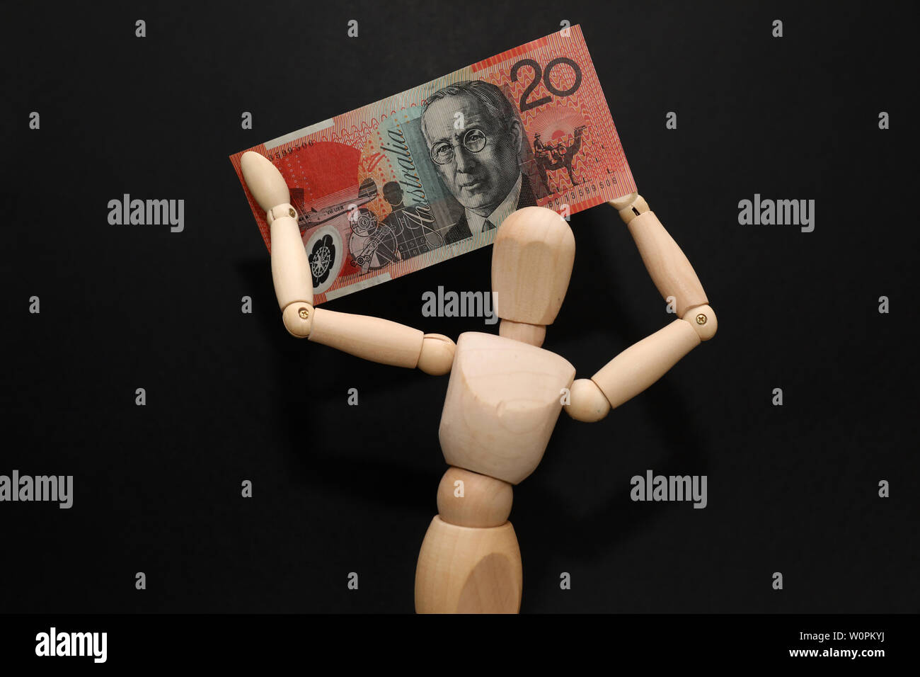 Une personne détenant un mannequin en bois de vingt dollars australien note ci-dessus sa tête. Fond noir. Concept de loterie gagnant. Maison de vacances voyage Banque D'Images