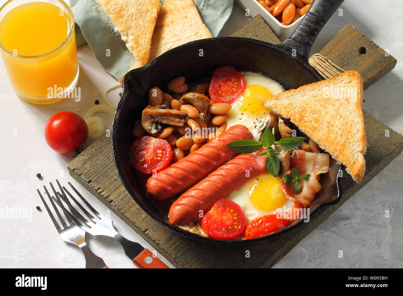 Petit-déjeuner en anglais oeufs brouillés avec bacon, haricots, champignons, saucisses, tomates et jus sur table en pierre. Banque D'Images