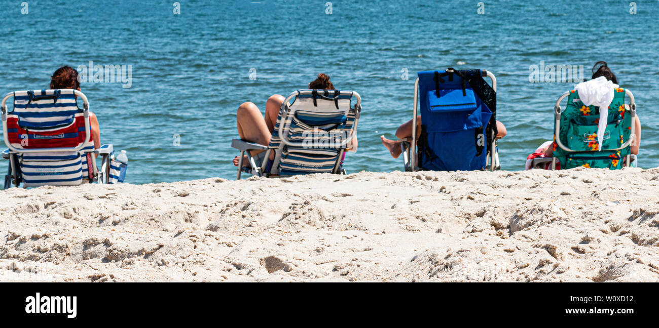 Vue de derrière de quatre femmes de détente dans les chaises de plage avec vue sur l'océan à la plage. Banque D'Images