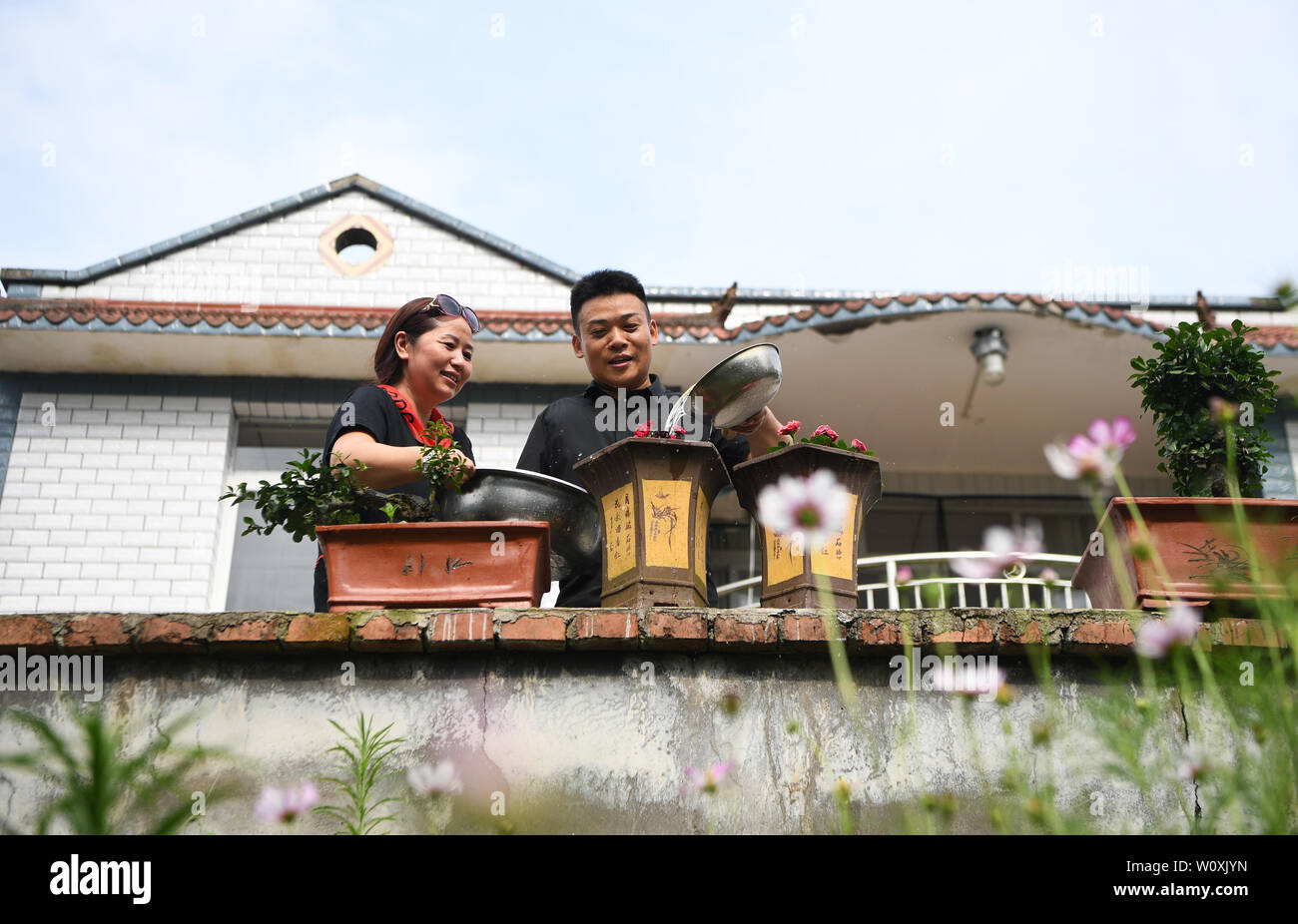 (190628) -- CHONGQING, 28 juin 2019 (Xinhua) -- Liu Yi (R) et son épouse Lu Kai fleurs d'eau dans la cour de leur maison à Nanchuan District, Chongqing, du sud-ouest de la Chine, 27 juin 2019. Malgré la perte de son bras droit dans un accident à l'âge de neuf ans, 44 ans, Liu Yi n'a jamais baissé la tête vers le destin. Après l'obtention du diplôme d'une école de formation professionnelle en 1994, il a essayé de nombreux emplois comme lave-vaisselle, fruits concessionnaire et mineur de charbon. Depuis 2010, il a décidé de démarrer sa propre entreprise à sa ville natale en organisant les villageois à planter des racines de bambou et d'élever des poulets. Les efforts qu'il a payé de Banque D'Images
