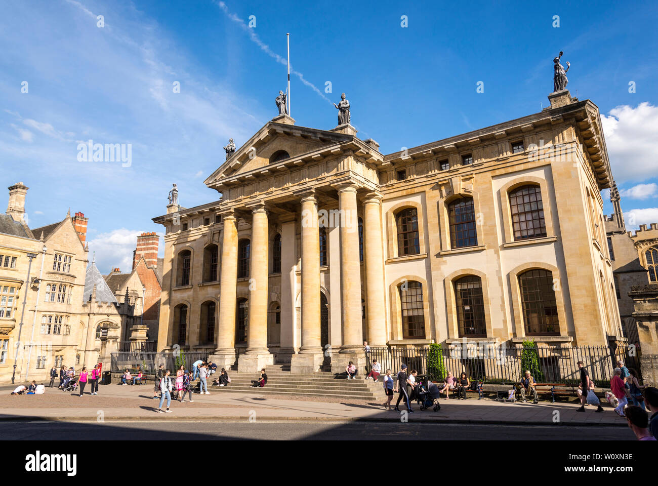 Les gens s'assoient sur les marches à l'avant du bâtiment Clarendon ensoleillée aux couleurs vives sur une belle journée d'été dans la célèbre ville universitaire d'Oxford Banque D'Images