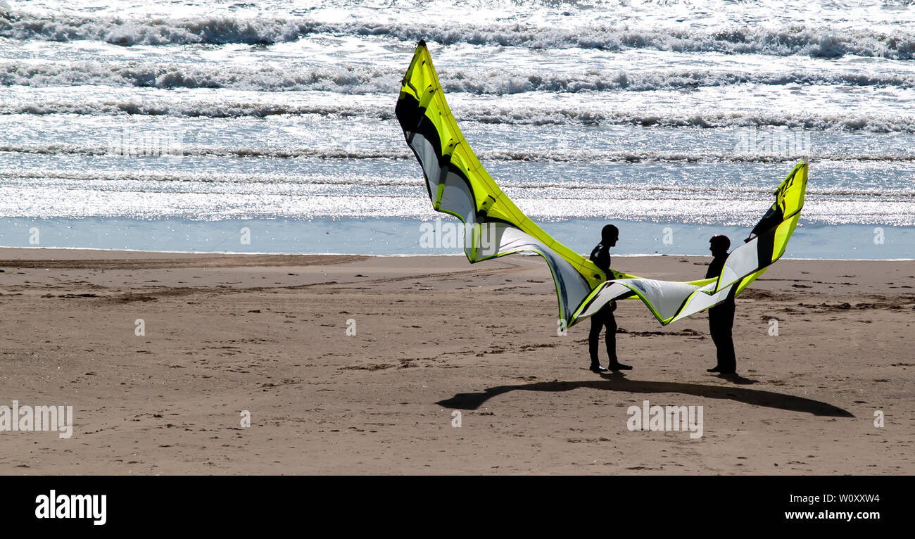 Kite surfeurs debout sur des sables bitumineux d'Aberavon holding sur un cerf-volant utilisé pour le kitesurf. Les vagues peuvent être vu briser sur la plage de sable. La Baie de Swansea. Banque D'Images