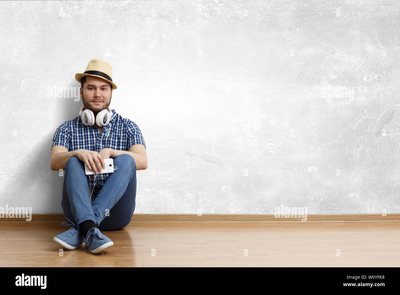 Jeune homme joyeux dans les tenues et un chapeau assis sur le plancher. Technique mixte Banque D'Images