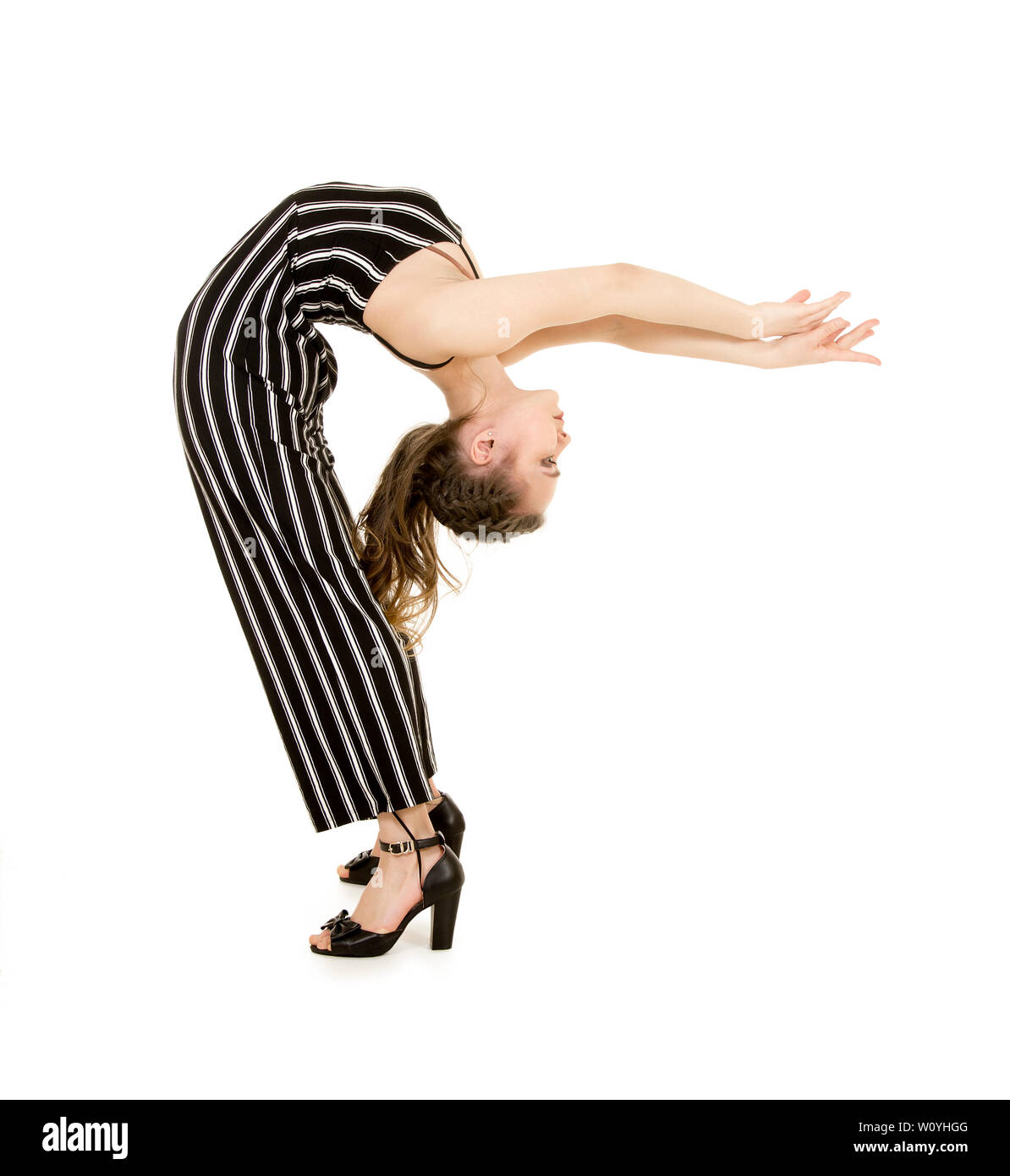 Une jeune femme souriante en costume rayé effectue des exercices gymnastiques et acrobatiques . Prise de vue en studio sur fond blanc. Banque D'Images