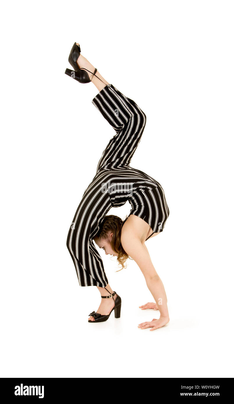 Une jeune femme souriante en costume rayé effectue des exercices gymnastiques et acrobatiques . Prise de vue en studio sur fond blanc. Banque D'Images