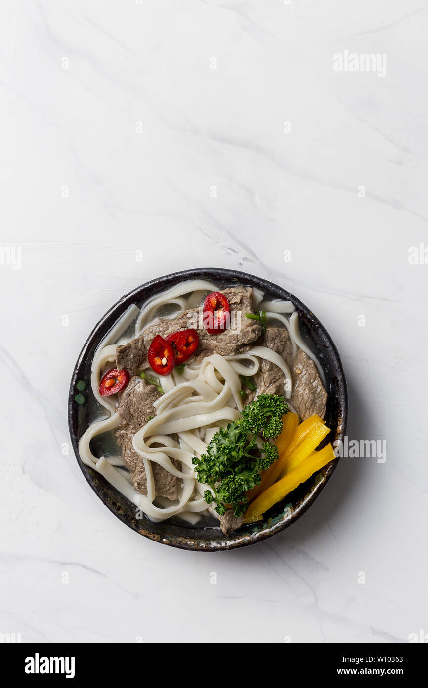 Soupe de nouilles chaudes avec le boeuf, l'oeuf, les champignons et les légumes dans un bol noir sur blanc en arrière-plan. L'espace de copie pour le texte. Banque D'Images Soupe de nouilles chaudes avec le boeuf, l'oeuf, les champignons et les légumes dans un bol noir sur blanc en arrière-plan. L'espace de copie pour le texte. Banque D'Images