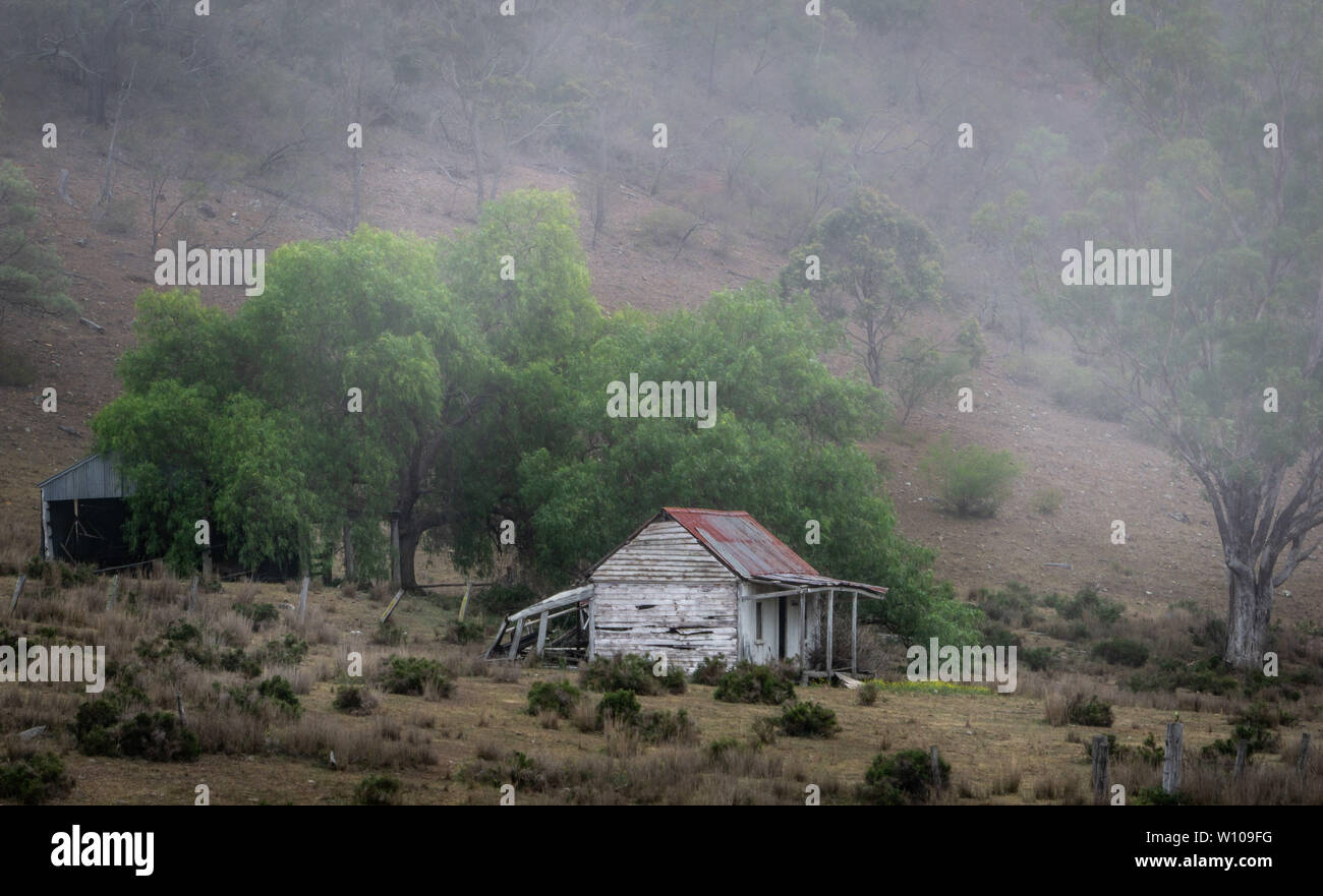 Ancienne maison de ferme australienne dans les collines avec pluie et brouillard roulant sur la colline Banque D'Images