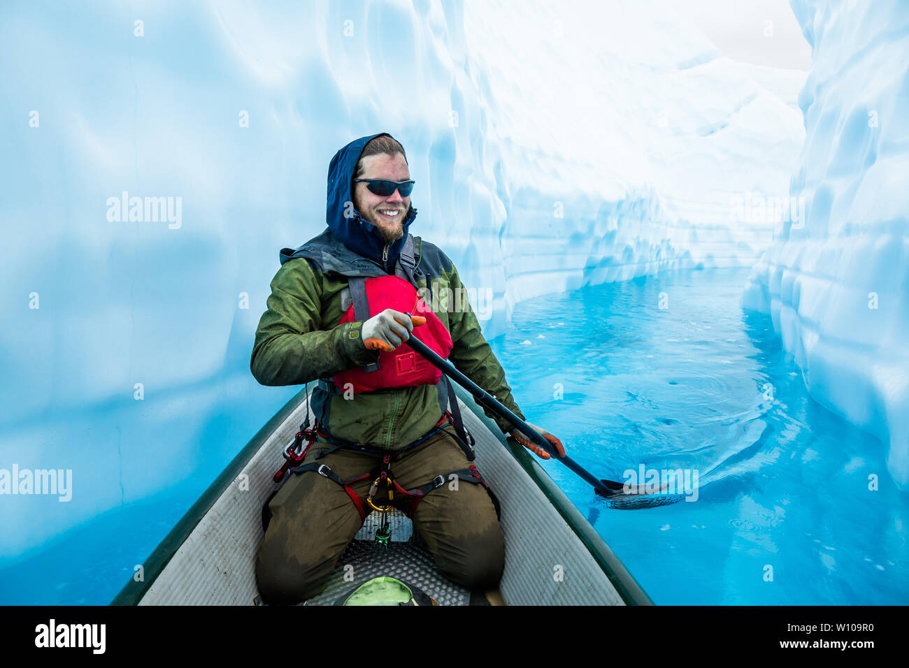 L'homme dans le faisceau à l'escalade de glace et de pagayage vfi un canoë gonflable à travers une crevasse remplie d'eau d'un bleu profond de la fonte du glacier. Banque D'Images