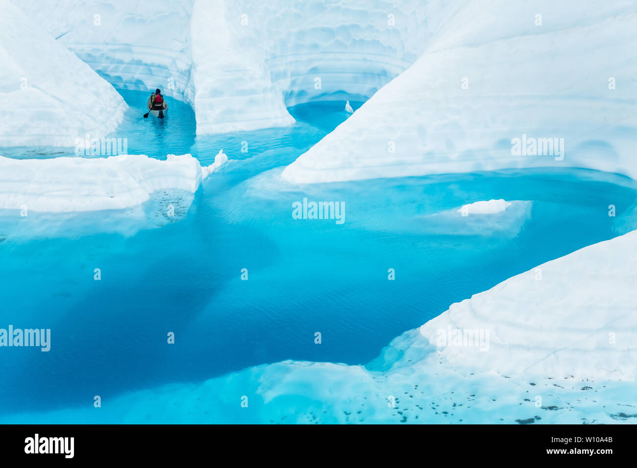 Un jeune homme paddles un canoë gonflable par nombreuses d'étroits canyons de glace. Les canyons sont coupées par la fonte de glaciers, plus tard inondé par massi Banque D'Images