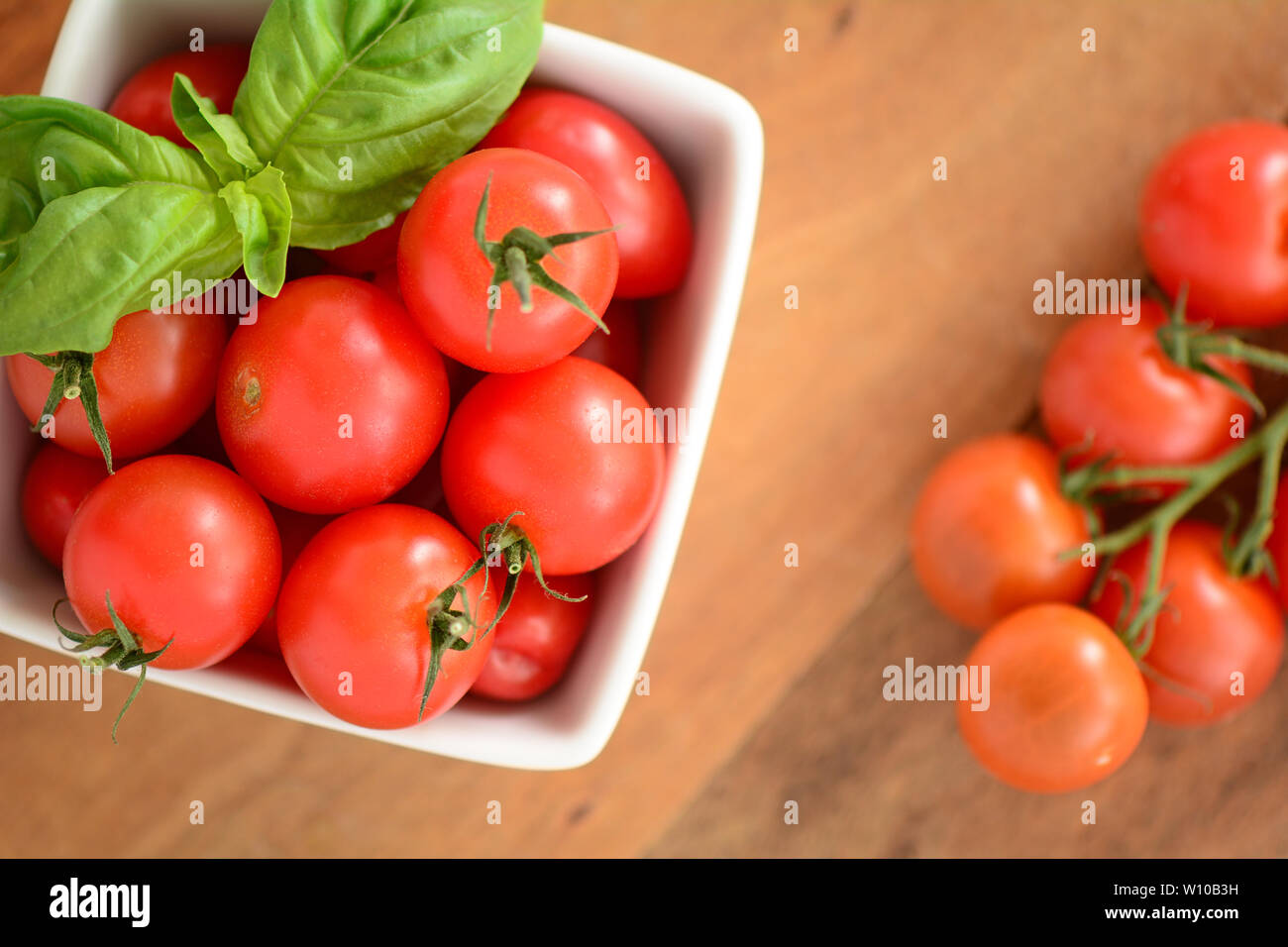 Tomates cerise bio cueillies fraîches avec des feuilles de basilic dans un plat carré blanc sur fond de bois. Concept de saine alimentation dans flatlay compositi Banque D'Images