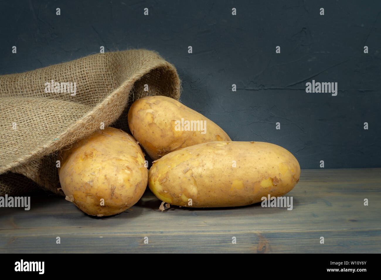 Matières, sans les laver, éplucher les pommes de terre, s'échappant de sac en toile de jute sur un vieux fond de bois rustique Banque D'Images
