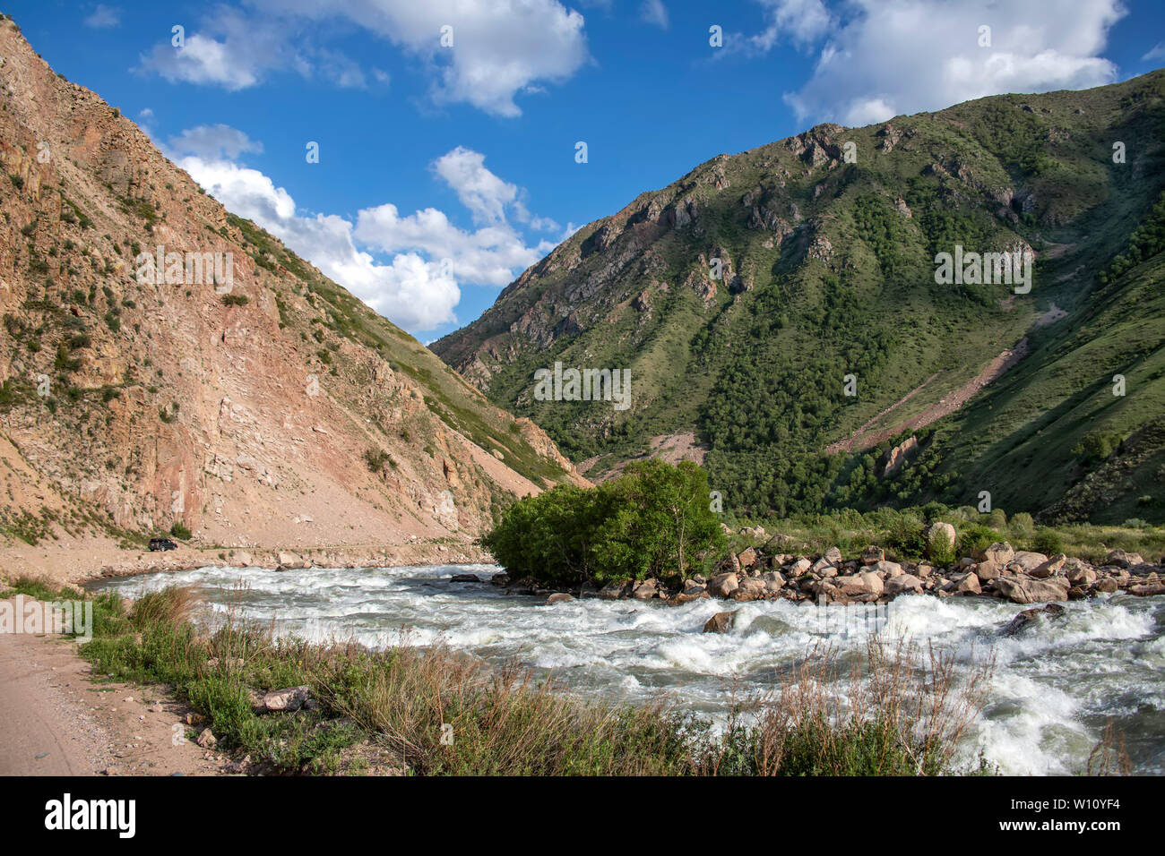 Rivière qui coule entre les vertes collines de neige sommets enneigés à l'horizon contre un ciel nuageux. Banque D'Images