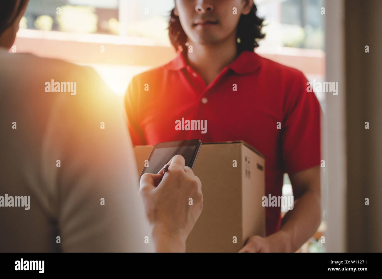 Jeune femme de l'ajout du client signature dans téléphone mobile numérique réception de colis postal fort de coursier avec service de livraison à domicile man smiling face Banque D'Images