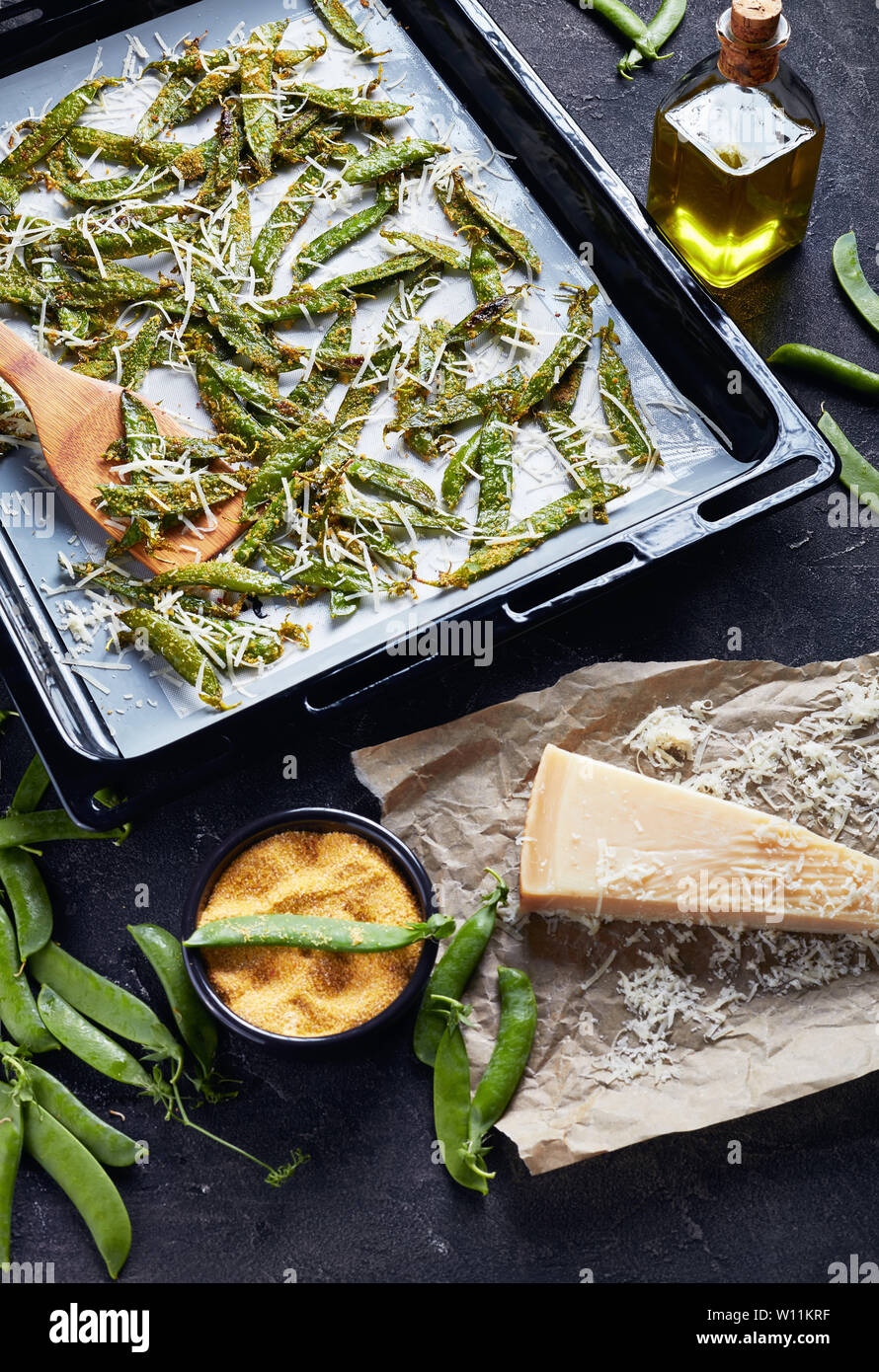 Croustillant de Parmesan et petits pois pané polenta rôtis dans un plat de cuisson. Ingrédients sur une table en béton, vertical Vue de dessus Banque D'Images