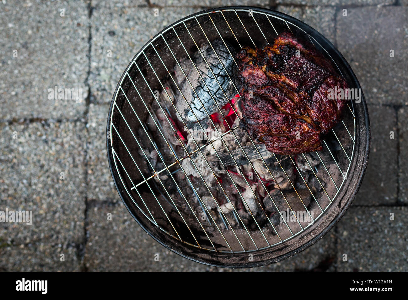 Une vue d'un grand de poitrine et d'être sur un petit barbecue grill chaufferette avec braise en dessous. Banque D'Images