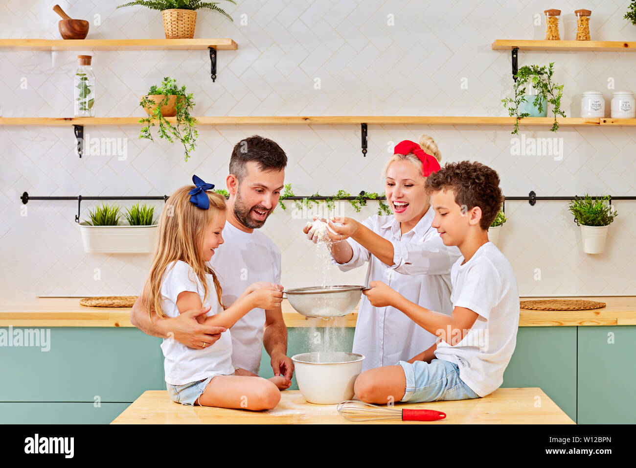 Famille heureuse dans la cuisine.Le père et les enfants préparent des cookies dans la cuisine. Verser la farine mère Banque D'Images