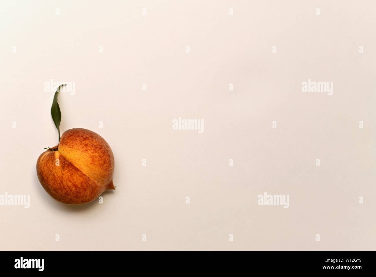 Ripe peach rouge-jaune avec vert feuille vers le haut. Avec une ombre légère en bas. Sur un fond clair ci-dessous à gauche. Banque D'Images