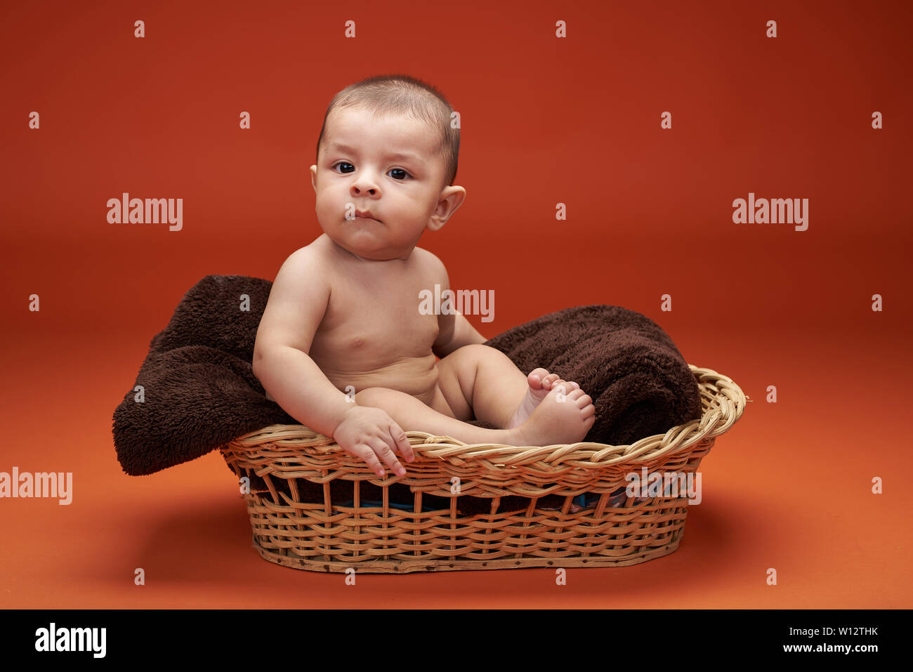 Petit bébé garçon dans panier assis et à la caméra en Banque D'Images