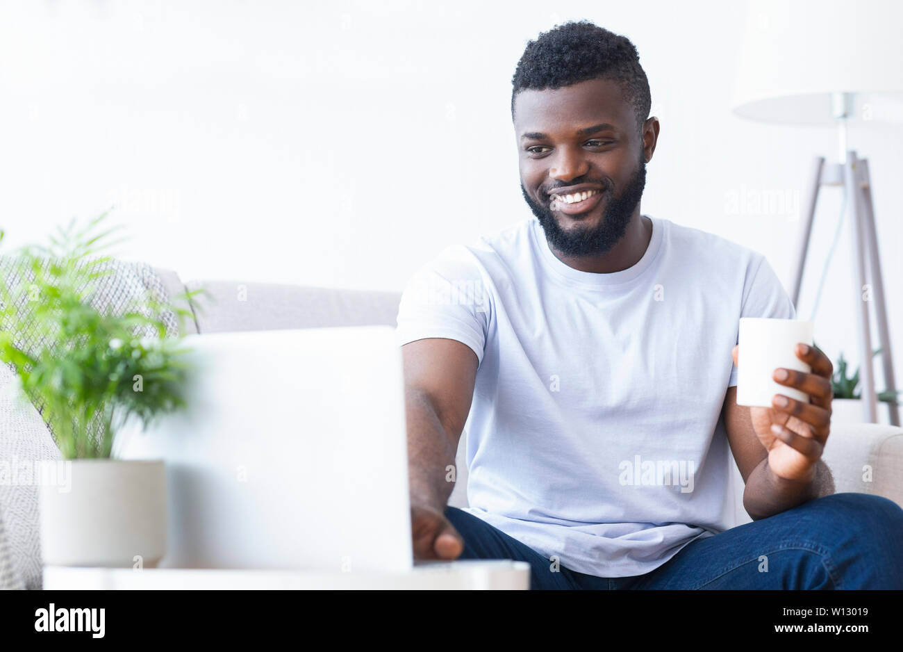Happy black guy working on laptop with coffee cup Banque D'Images