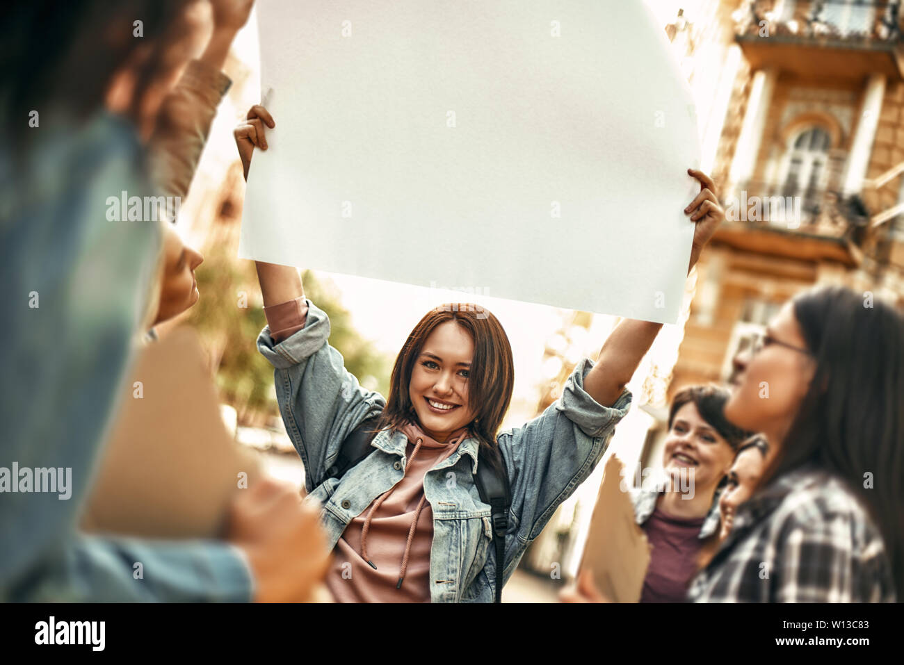 Les femmes de pouvoir. Happy young woman holding blank sign board sur sa tête et sourit tout en se tenant sur la route autour d'autres militantes. Les droits de l'homme. Concept de protestation Banque D'Images