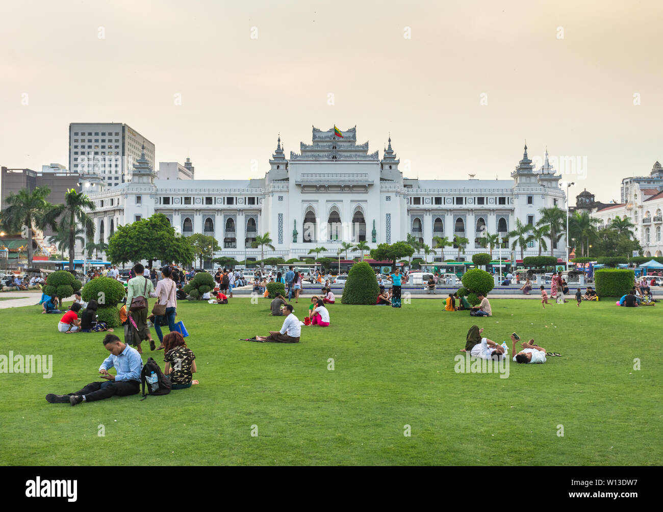 Des gens assis sur l'herbe dans Maha Bandula parc en face de Yangon City Hall Building à la Birmanie. Banque D'Images