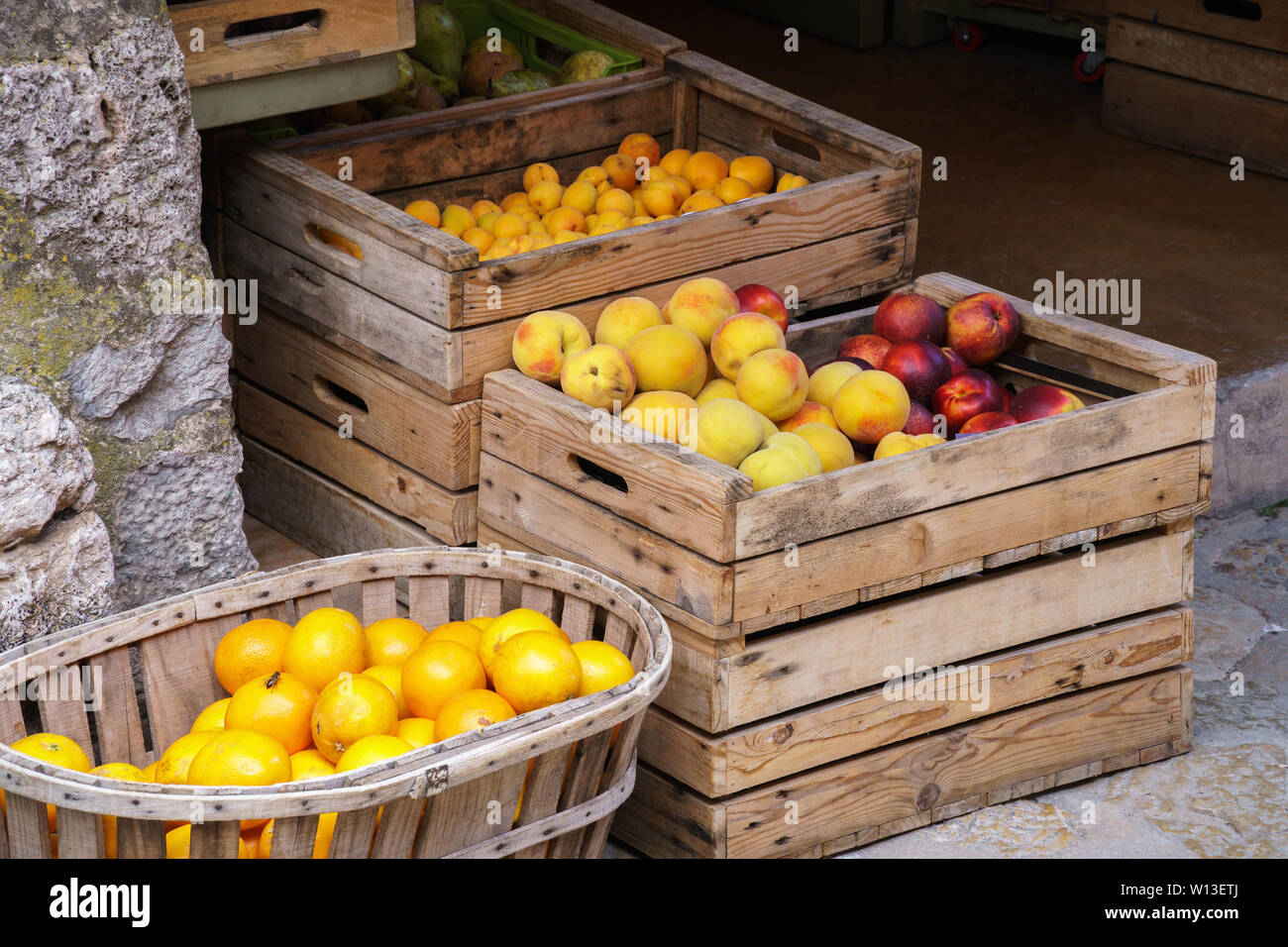 Oranges mûres, pêches, nectarines, prunes jaunes et les poires dans des caisses en bois et d'un panier à un marché d'alimentation, une séance d'abeilles sur les oranges - Vue du côté incliné Banque D'Images