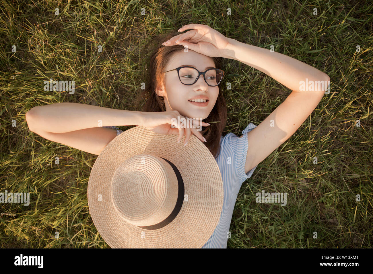 Close-up Vue de dessus d'une jeune fille dans le parc étendu sur l'herbe verte. Lunettes et chapeau. Jeunesse et loisirs loisirs heureux Banque D'Images