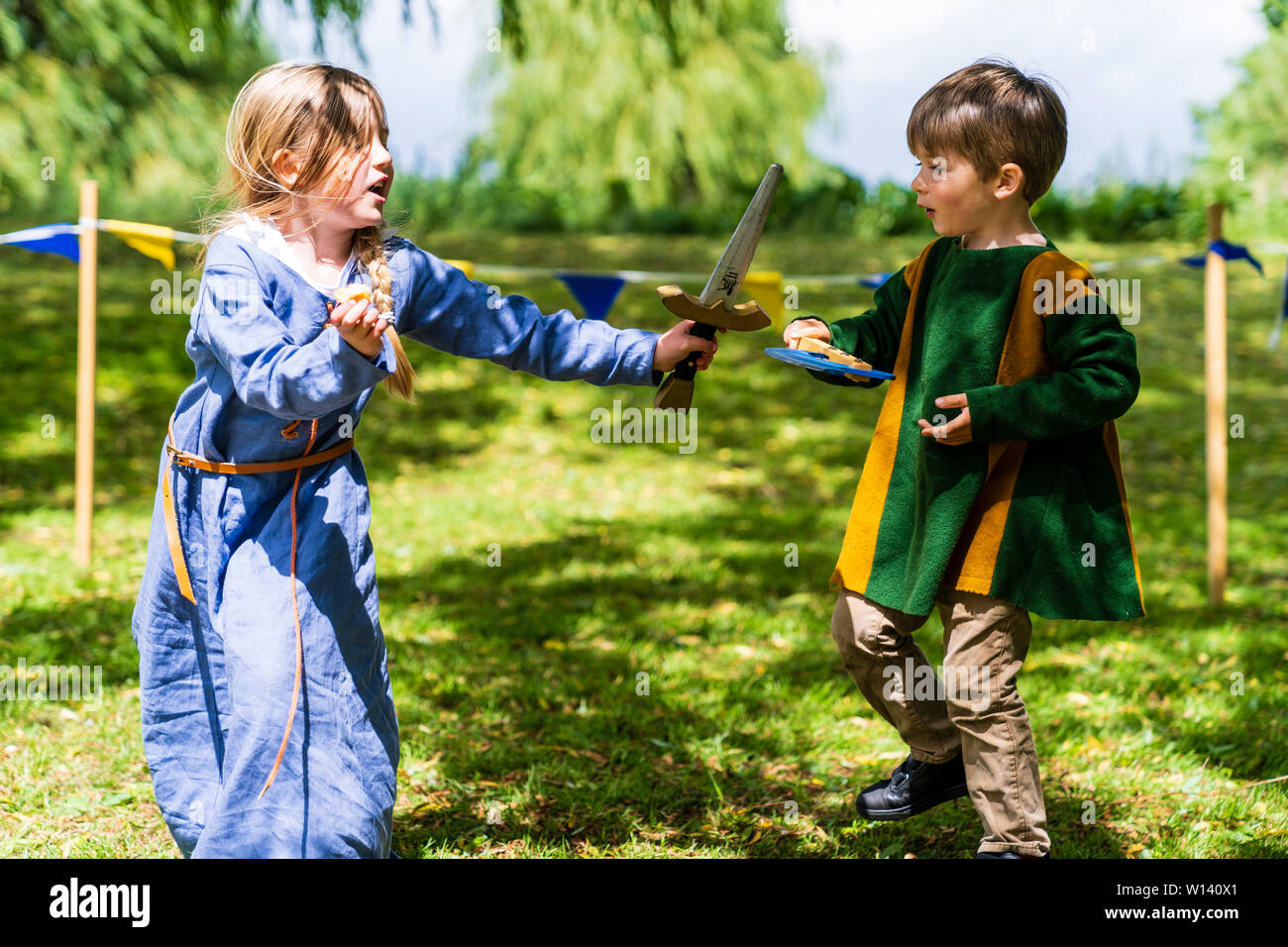 Deux enfants, garçon, 4-5 ans, et une fille, 5-6 ans, vêtu de vêtements médiévaux et les combats de manière ludique à l'épée et hache sur l'herbe. Banque D'Images