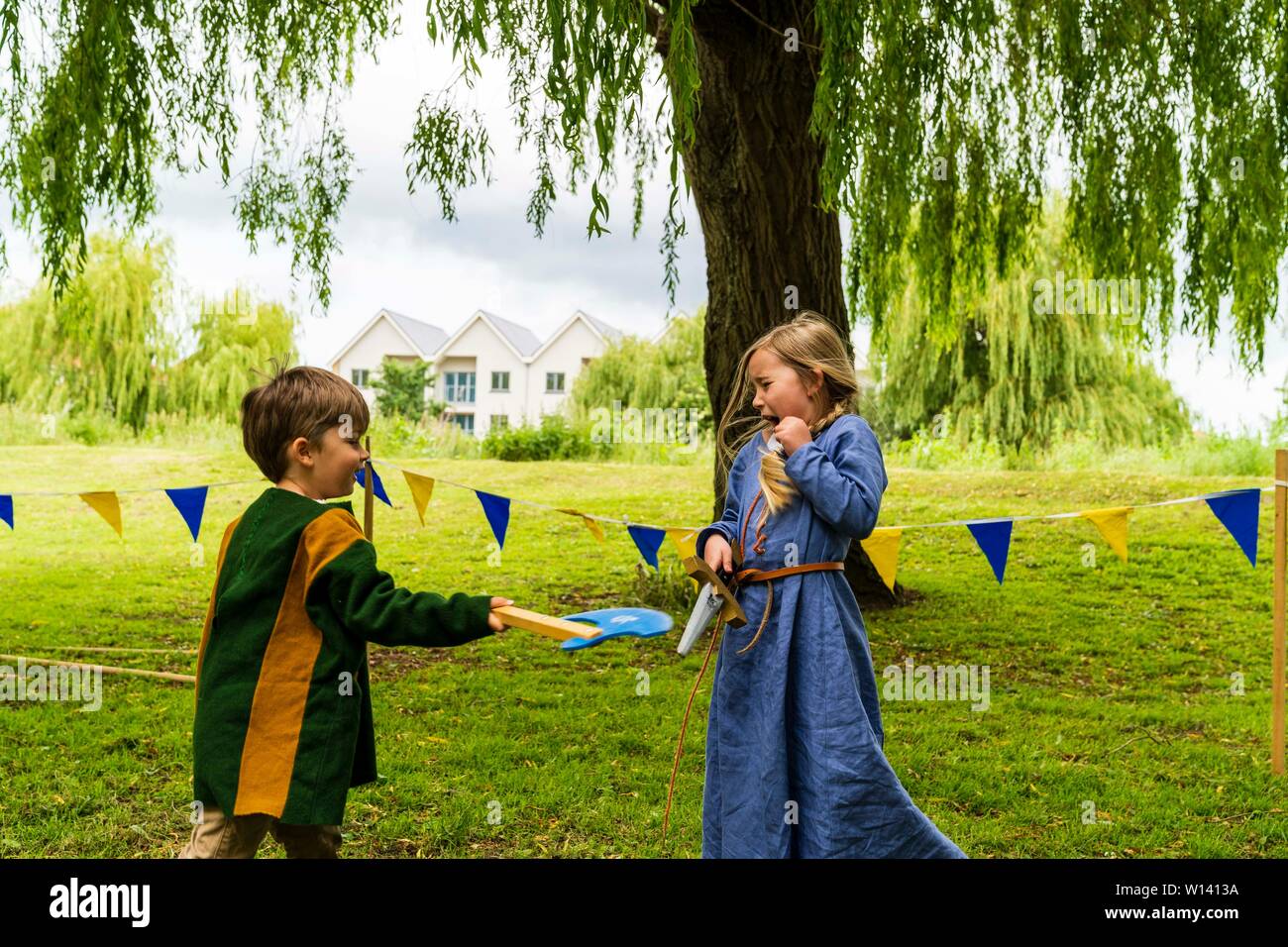Deux enfants, garçon, 4-5 ans, et une fille, 5-6 ans, vêtu de vêtements médiévaux et les combats de manière ludique à l'épée et hache sur l'herbe. Banque D'Images