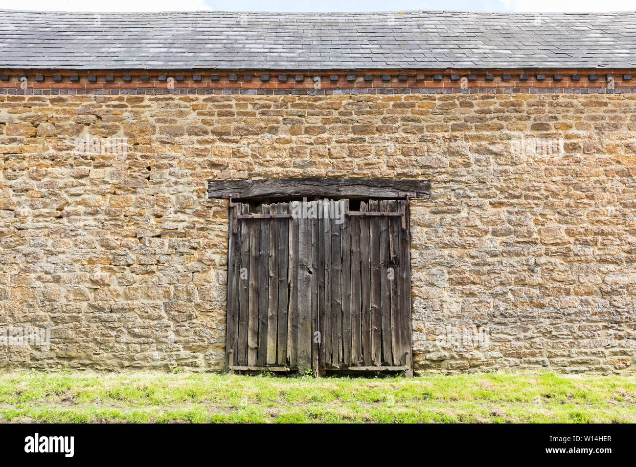 Watford, Northamptonshire, Royaume-Uni : portes en bois doubles délabrées, dépourvues de murs d'une grange en pierre avec un toit en ardoise. Banque D'Images
