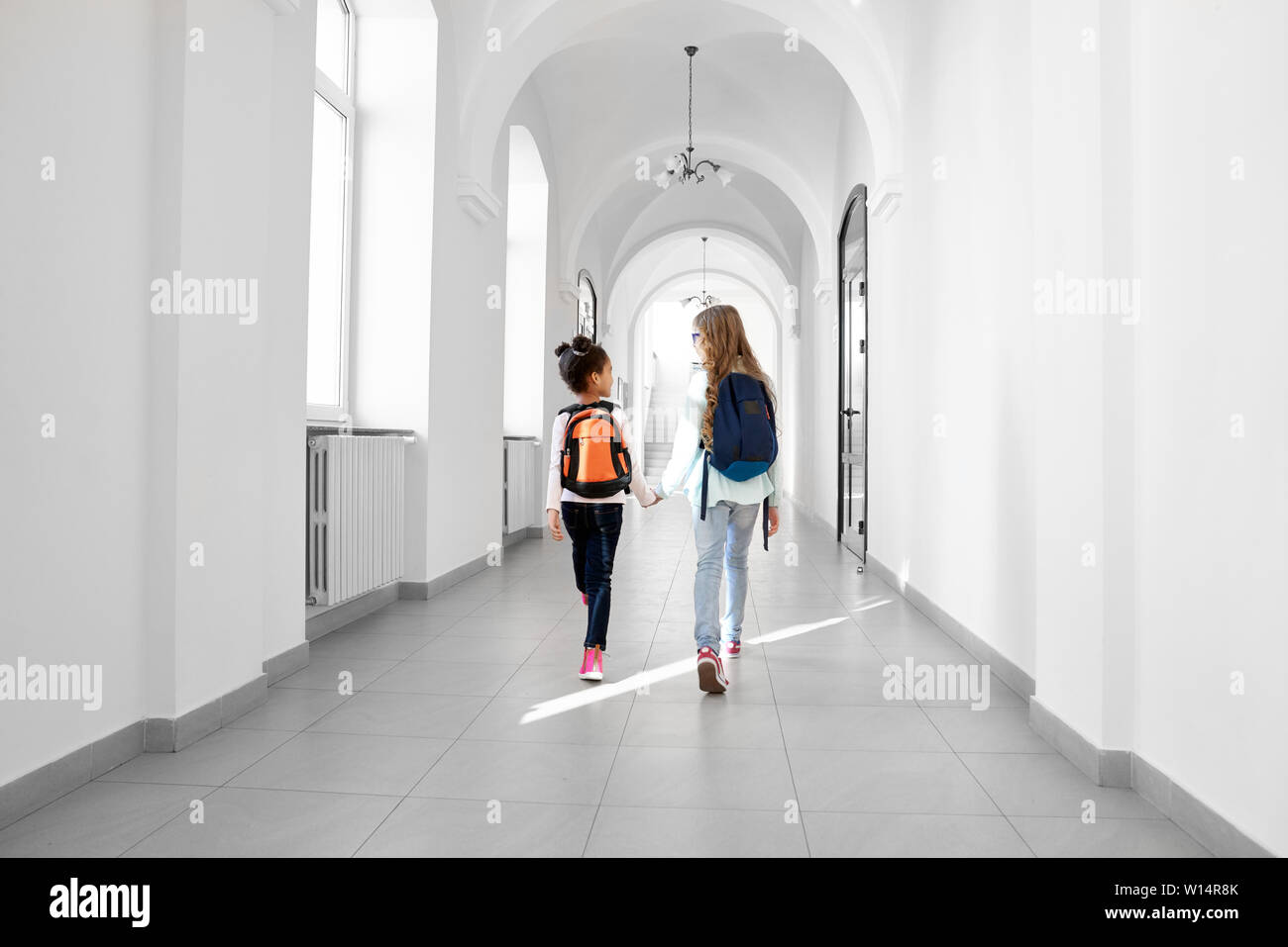 Vue arrière de deux jeunes filles à l'avenir au couloir d'école avec des sacs sur le dos. Fille de l'école deux amis Aller accueil à partir de leçons. Concept de l'étude dans la belle école. Banque D'Images