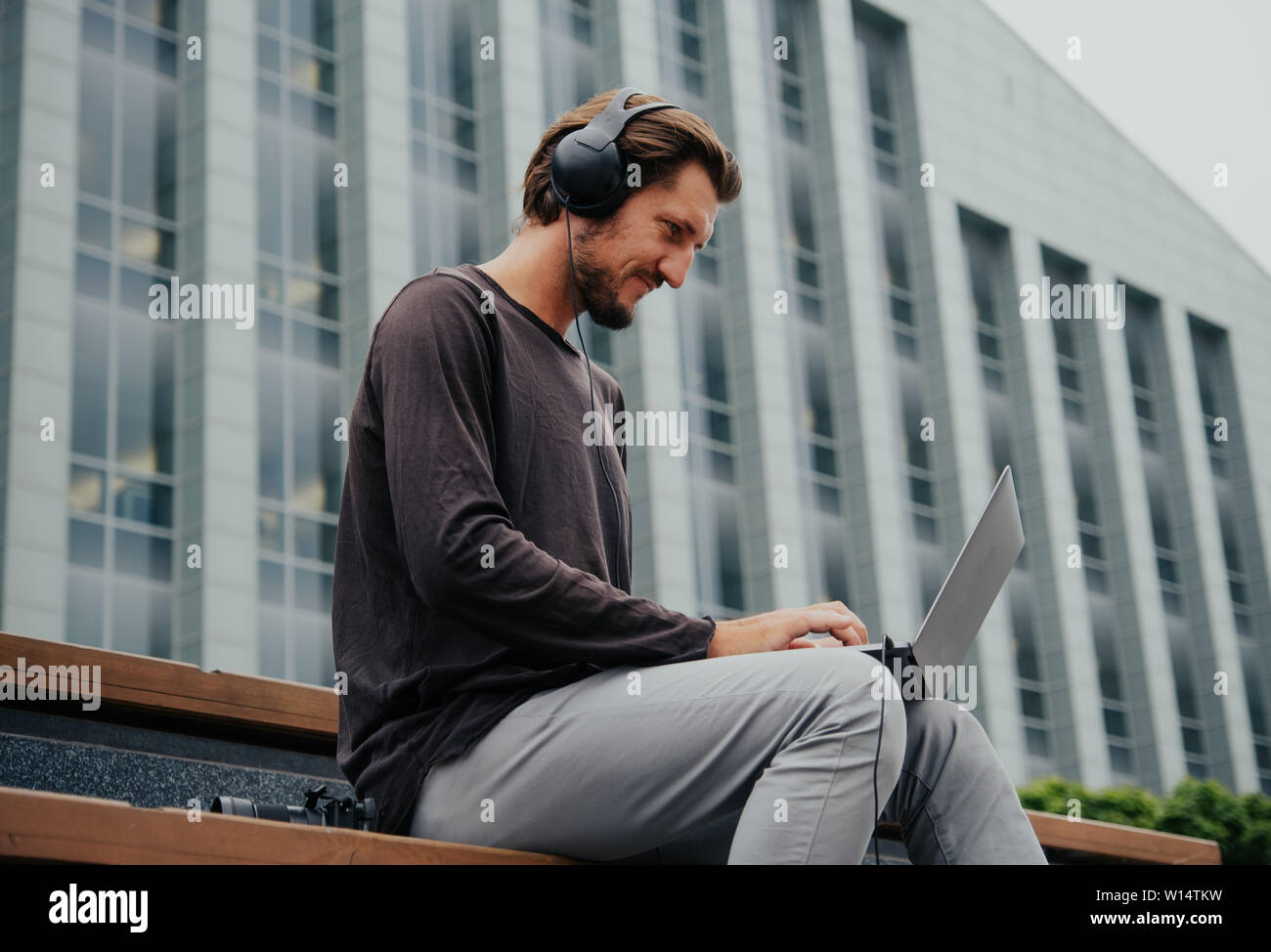 Les offres de guy écoute de la musique sur le casque, et sac travaille sur un ordinateur portable au centre d'une grande ville. Banque D'Images