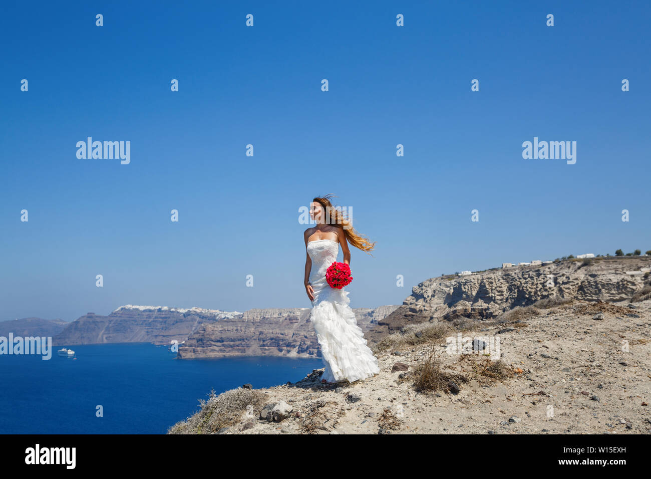 Belle femme dans une robe blanche se tient sur une falaise et regarde la mer, la Grèce, l'île de Santorin. Banque D'Images