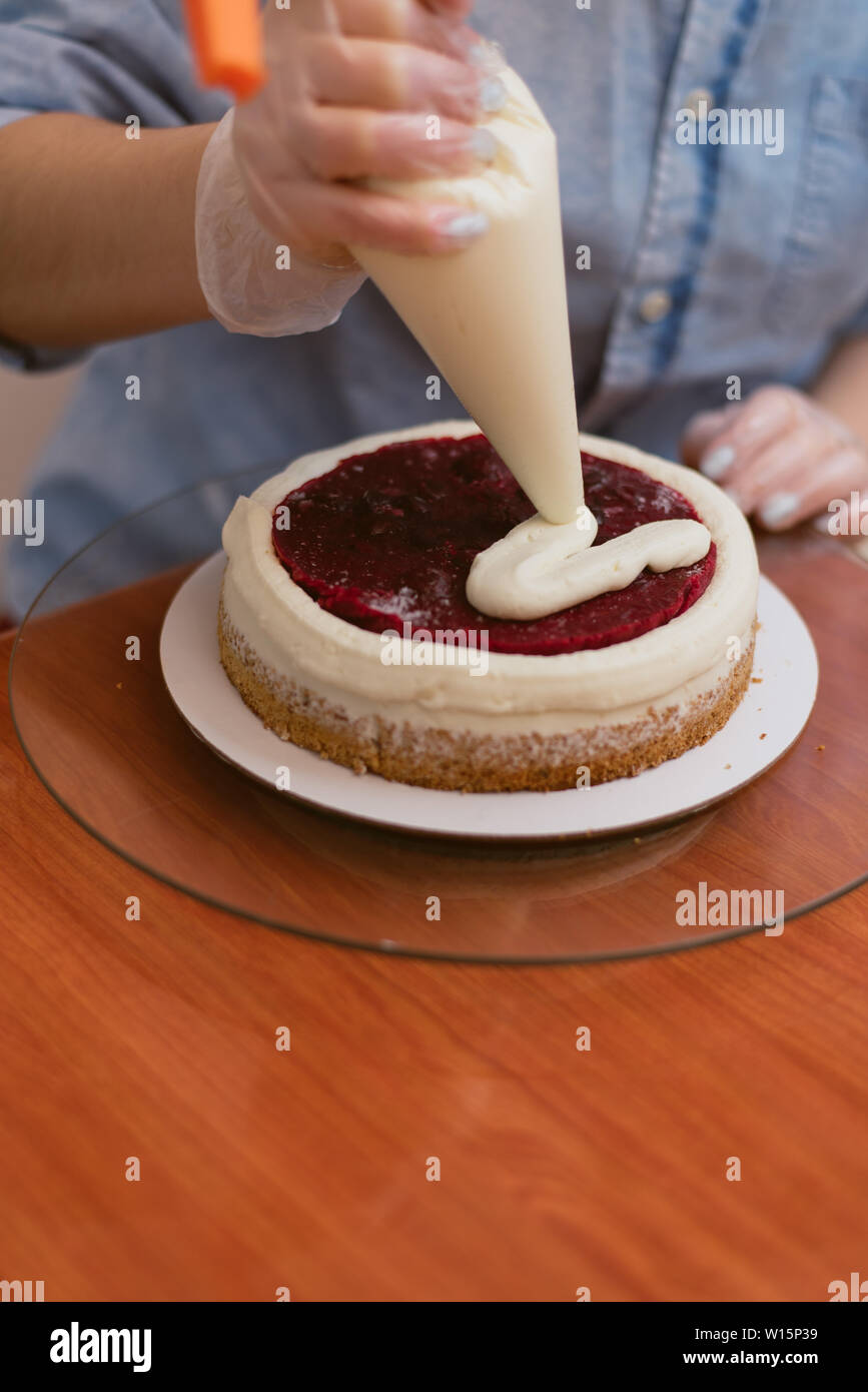 Une Jolie Fille Faire Un Gateau Dans Une Boulangerie Baker Comprime Creme Sur Un Gateau Rouge En Blanc Gateau Blanc Sur Une Table En Bois Photo Stock Alamy