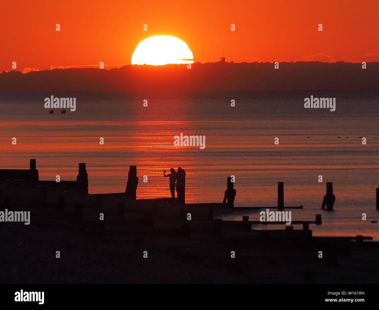 Minster sur Mer, Kent, UK. 30 Juin, 2019. Météo France : le coucher du soleil à Minster sur Mer, Kent à la fin de journée chaude et humide. Une femme prend un de selfies un brise-lames. Credit : James Bell/Alamy Live News Banque D'Images