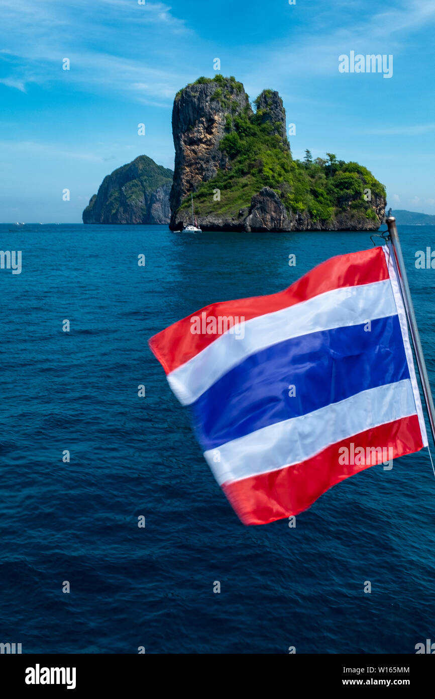 Un portrait d'un marin d'une petite île thaïlandaise de calcaire dans les eaux scintillantes de la mer d'Andaman, avec le drapeau de la Thaïlande palpitations dans l'foregro Banque D'Images