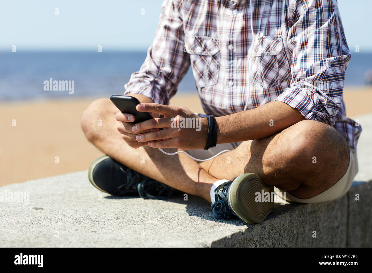 Mid section portrait of young man using smartphone contemporain assis sur des blocs de béton par mer, copy space Banque D'Images