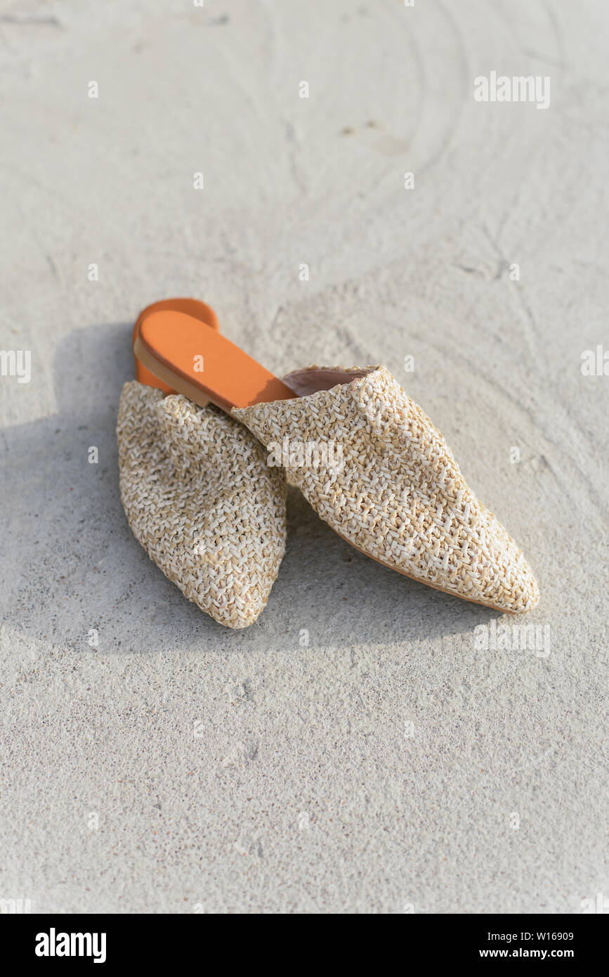 Fashion beige mules en osier sur l'arrière-plan d'asphalte et de béton, l'été et l'élégant. chaussures tendance sans que personne. Banque D'Images