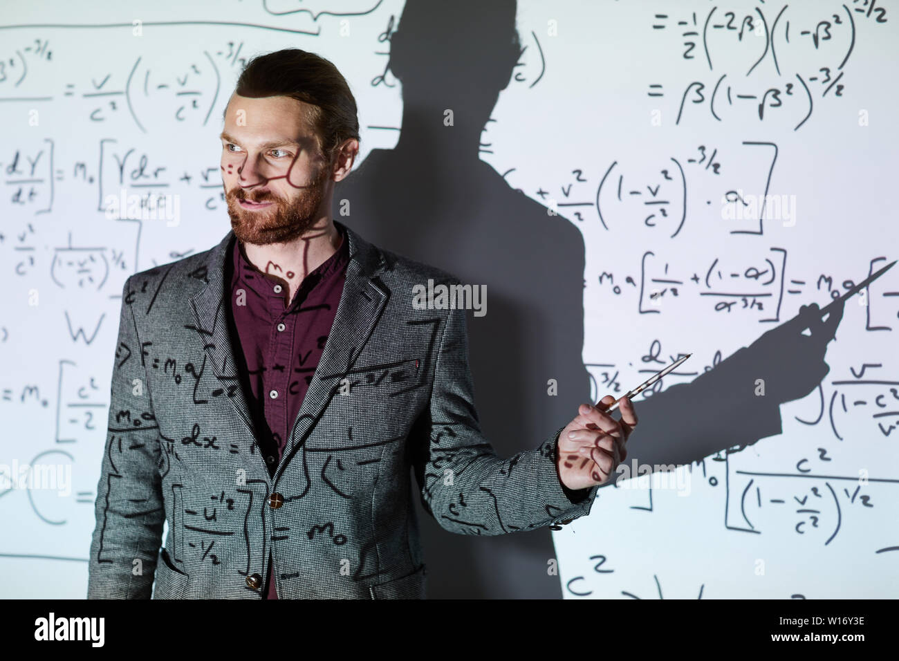 Content confiant professeur de mathématiques de barbu en veste debout contre l'écran de projection et en montrant les calculs tout en expliquant la formule Banque D'Images