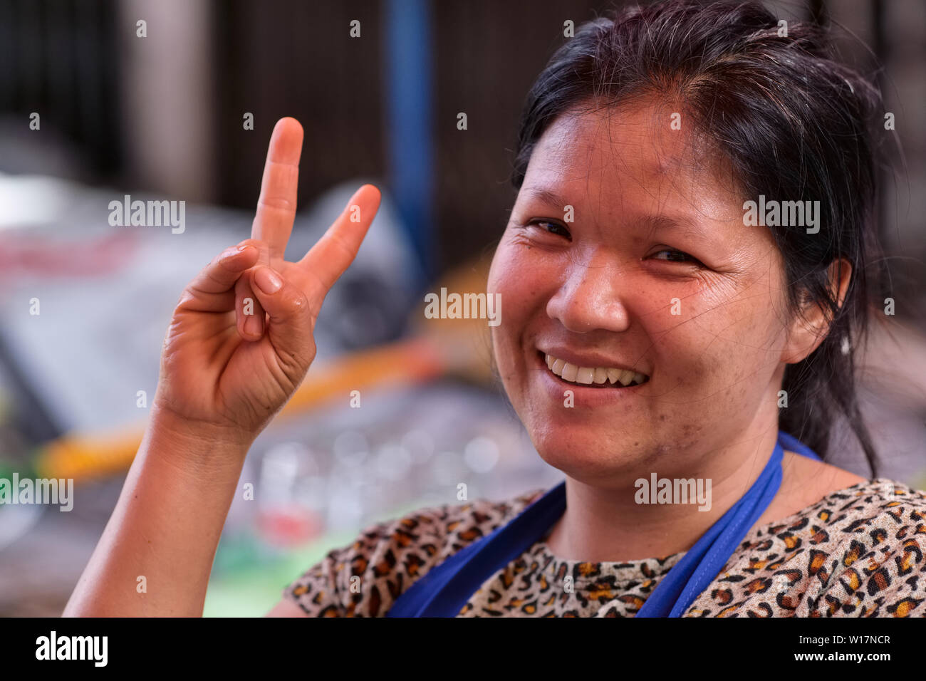 Un vendeur du marché thaïlandais femelle clignotant joyeusement l'omniprésent V ou la victoire, très populaire en Thaïlande Banque D'Images