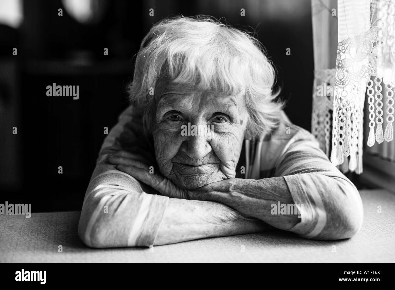 Close-up portrait noir et blanc d'une vieille femme à la table dans la maison. Banque D'Images