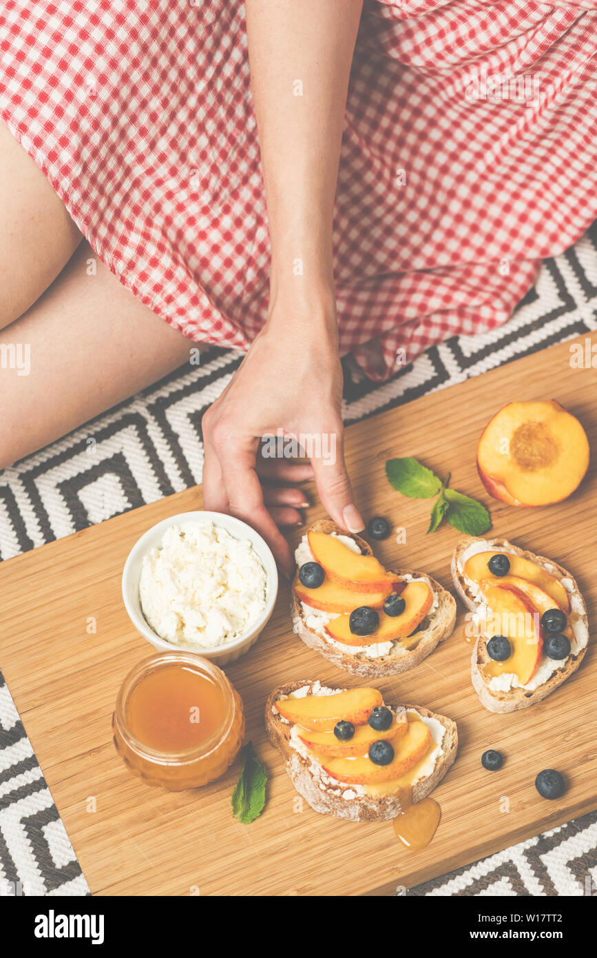 Fille sur la consommation de fruits pique-nique bruschetta avec baguette grillées, fromage ricotta, douce douce pêche juteuse, de bleuets et de miel. Concept de la santé, de l'été Banque D'Images