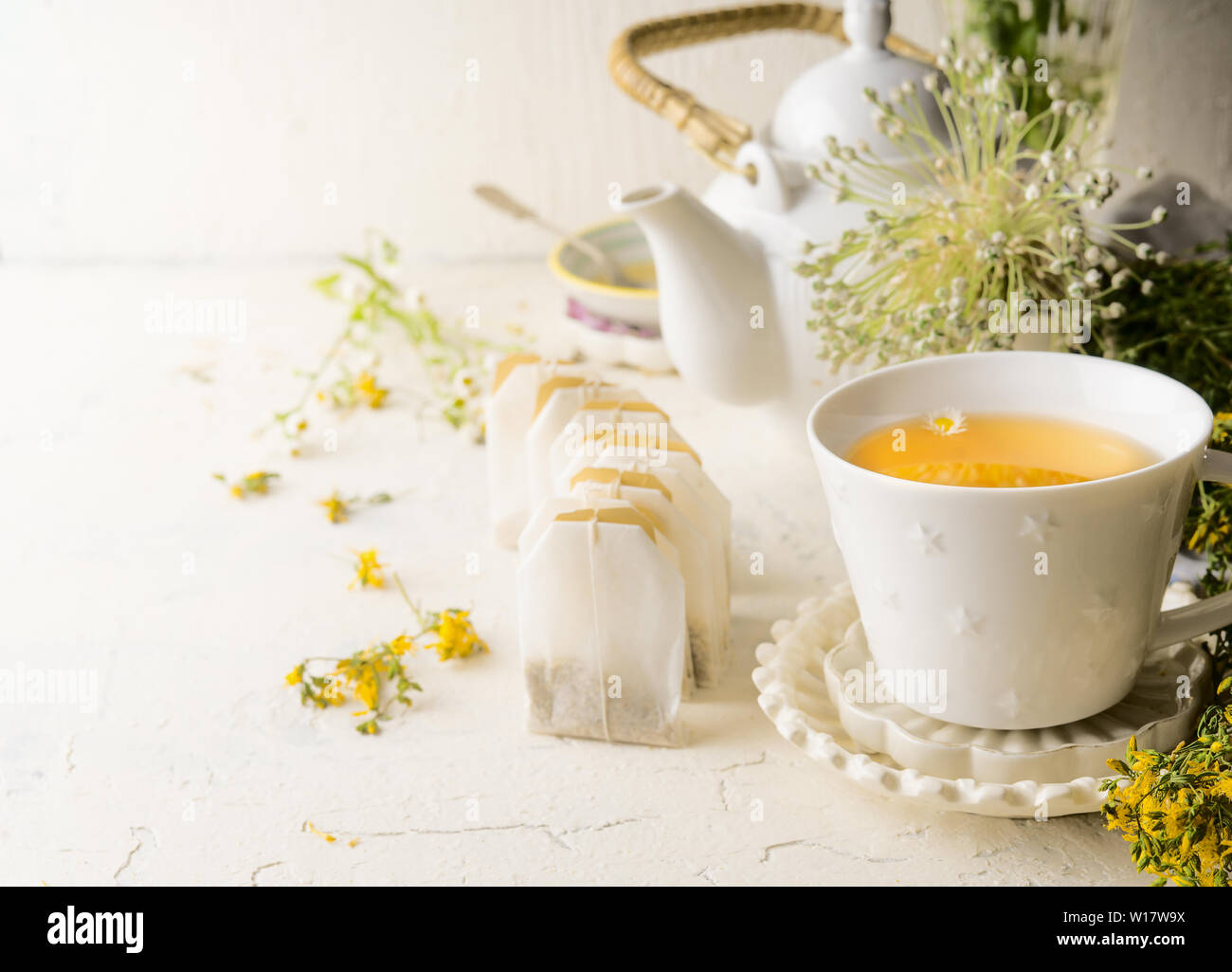Tasse de thé blanc avec des sachets de thé de thé de fines herbes debout sur le tableau blanc avec une théière et des plantes médicinales et de fleurs. Close up. Verre de prévention en santé Banque D'Images