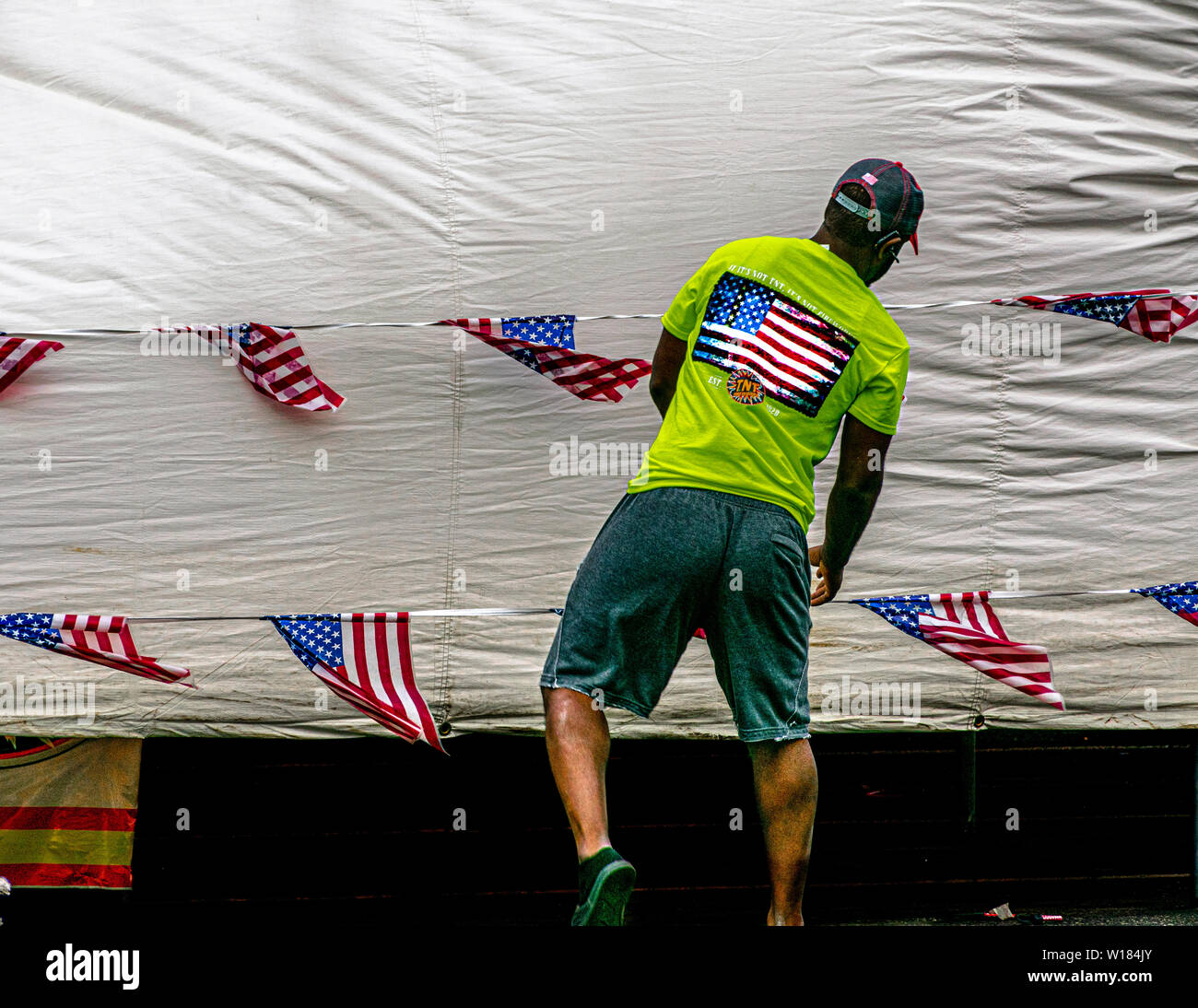 Un homme portant un tee-shirt avec un drapeau américain se trouve devant une ligne de vêtements dont plusieurs petits drapeaux américains sont accroché. Banque D'Images