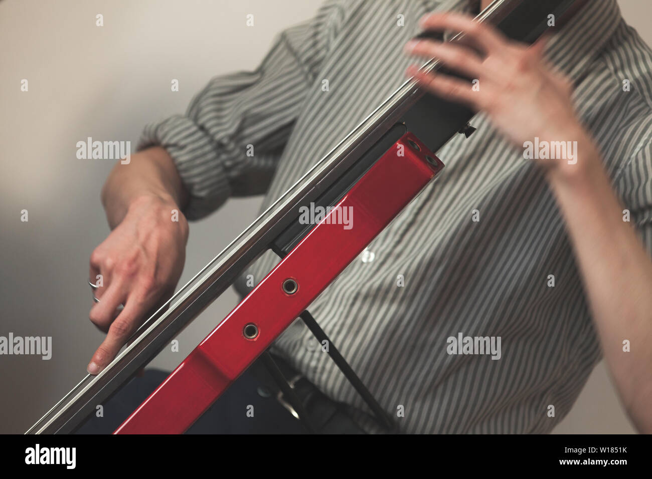 Arrière-plan de la musique live, les mains d'un homme jouant de la contrebasse électrique moderne rouge. Photo en gros plan avec selective focus Banque D'Images