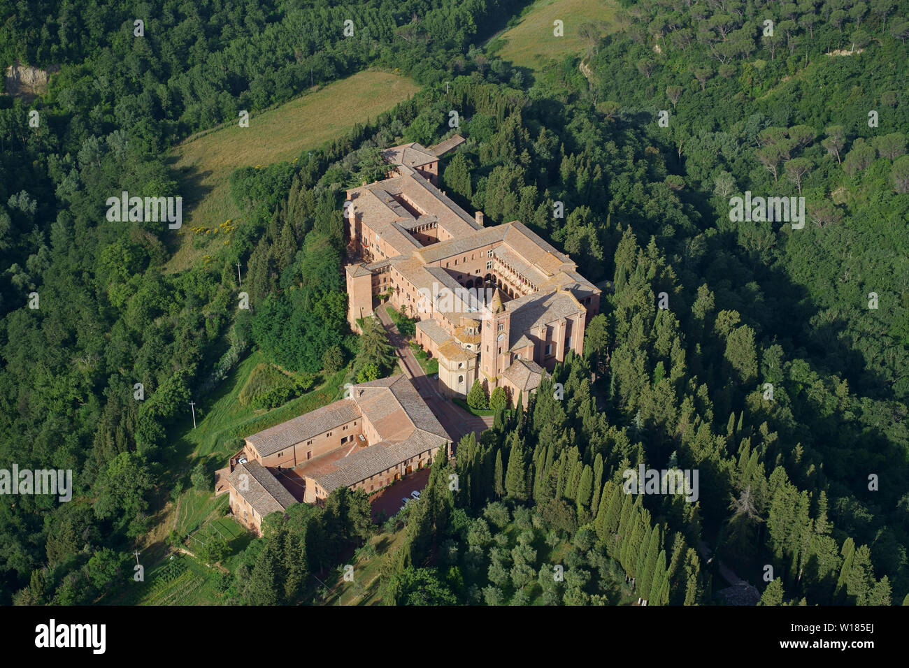 VUE AÉRIENNE. Abbaye isolée dans un cadre de collines boisées. Abbaye de Monte Oliveto Maggiore, Asciano, province de Sienne, Toscane, Italie. Banque D'Images